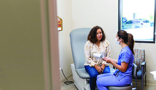 A female patient sitting in a doctor's chair speaking with a female healthcare professional.