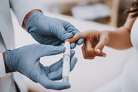 laboratorian's hands in blue gloves holds patient's finger to take a fingerstick blood sample