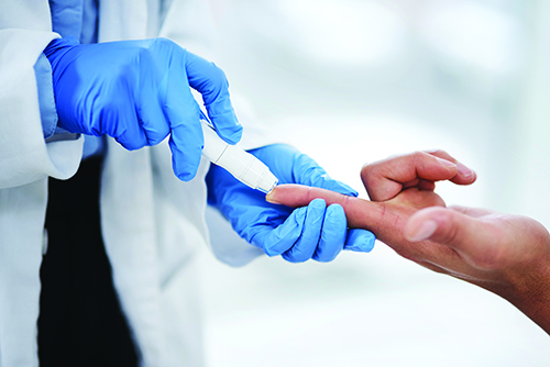 A closeup of a laboratorian's hands in blue gloves finger pricking a patient