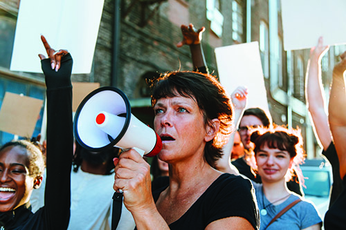 A woman holding a megaphone with protesters around her holding signs.