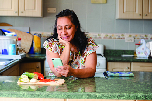A Hispanic woman leaning on a kitchen counter while looking at her phone.