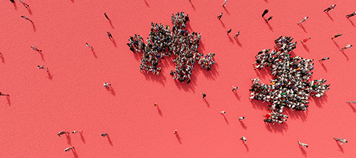 A birds-eye view of a crowd of people forming two separate puzzle pieces in front of a red background