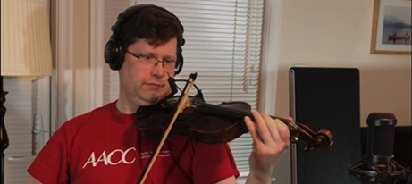 Stephen Master, a member of The Occasionals in a red AACC t-shirt playing the violin.