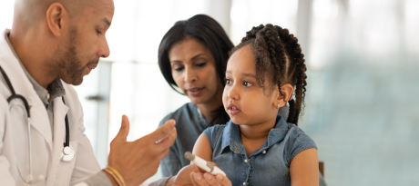 A doctor holding a point-of-care glucose test while talking with a little girl and her mother